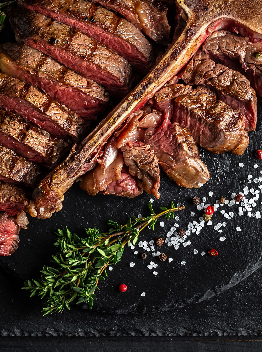 Gran filete tomahawk de ternera a la parrilla servido sobre una tabla de madera y guarnición de hierbas y sal marina.